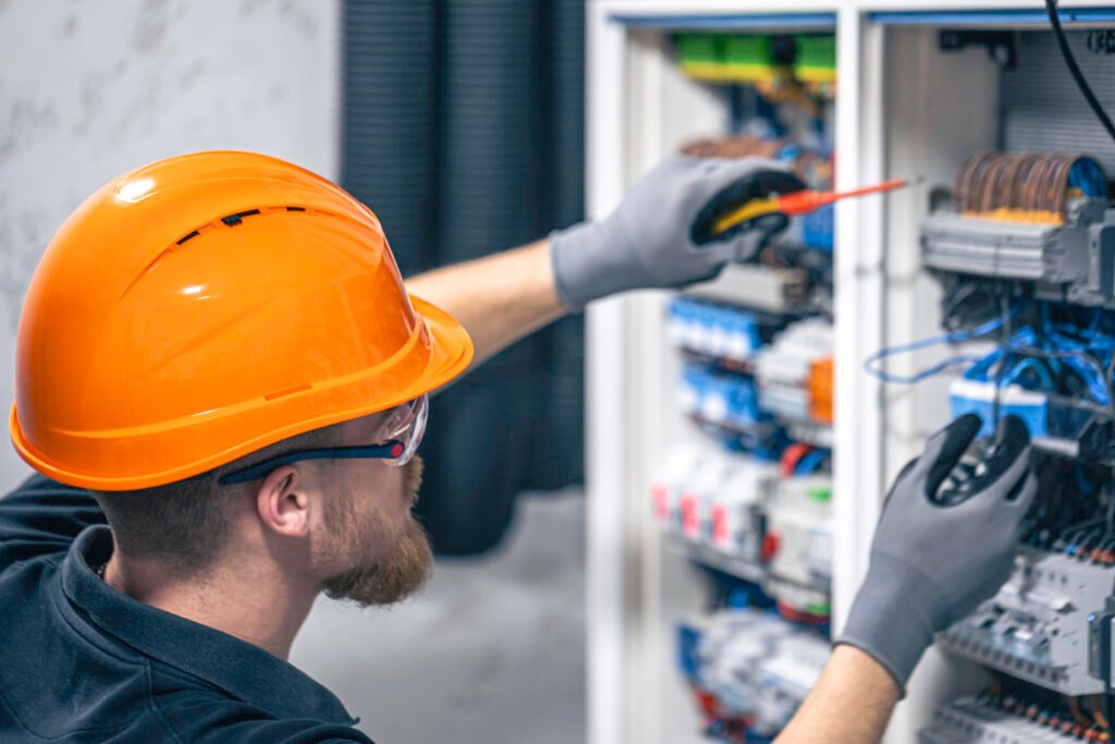 A male electrician works in a switchboard with an electrical connecting cable.